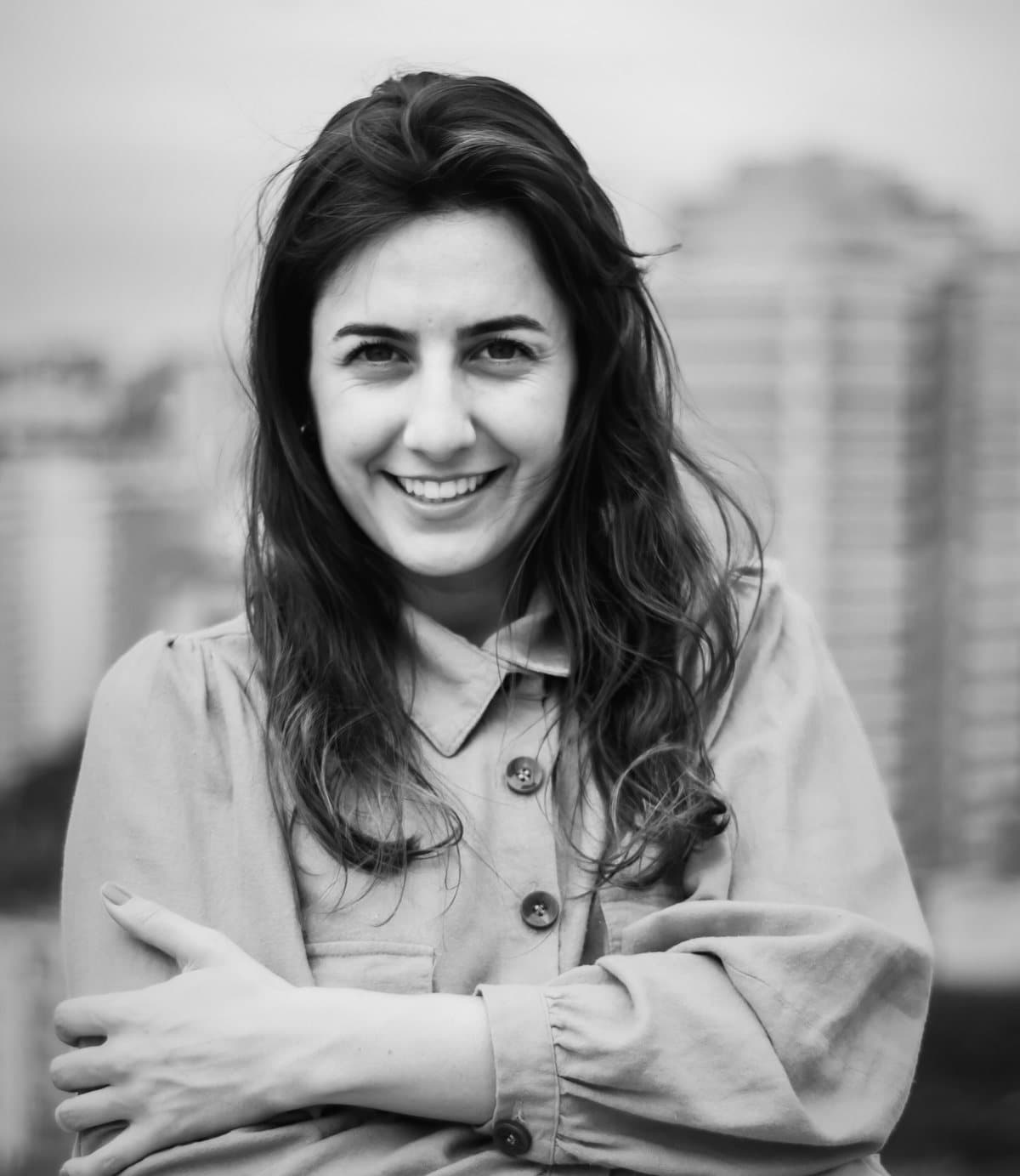 Alessandra R. Monteiro de braços cruzados, sorrindo, com a cidade desfocada ao fundo